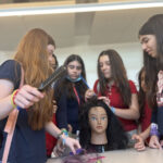 Several girls standing around a mannequin practicing hair styling