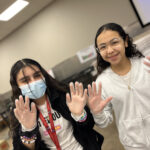 Two girls standing and holding up their hands, smiling at the photographer