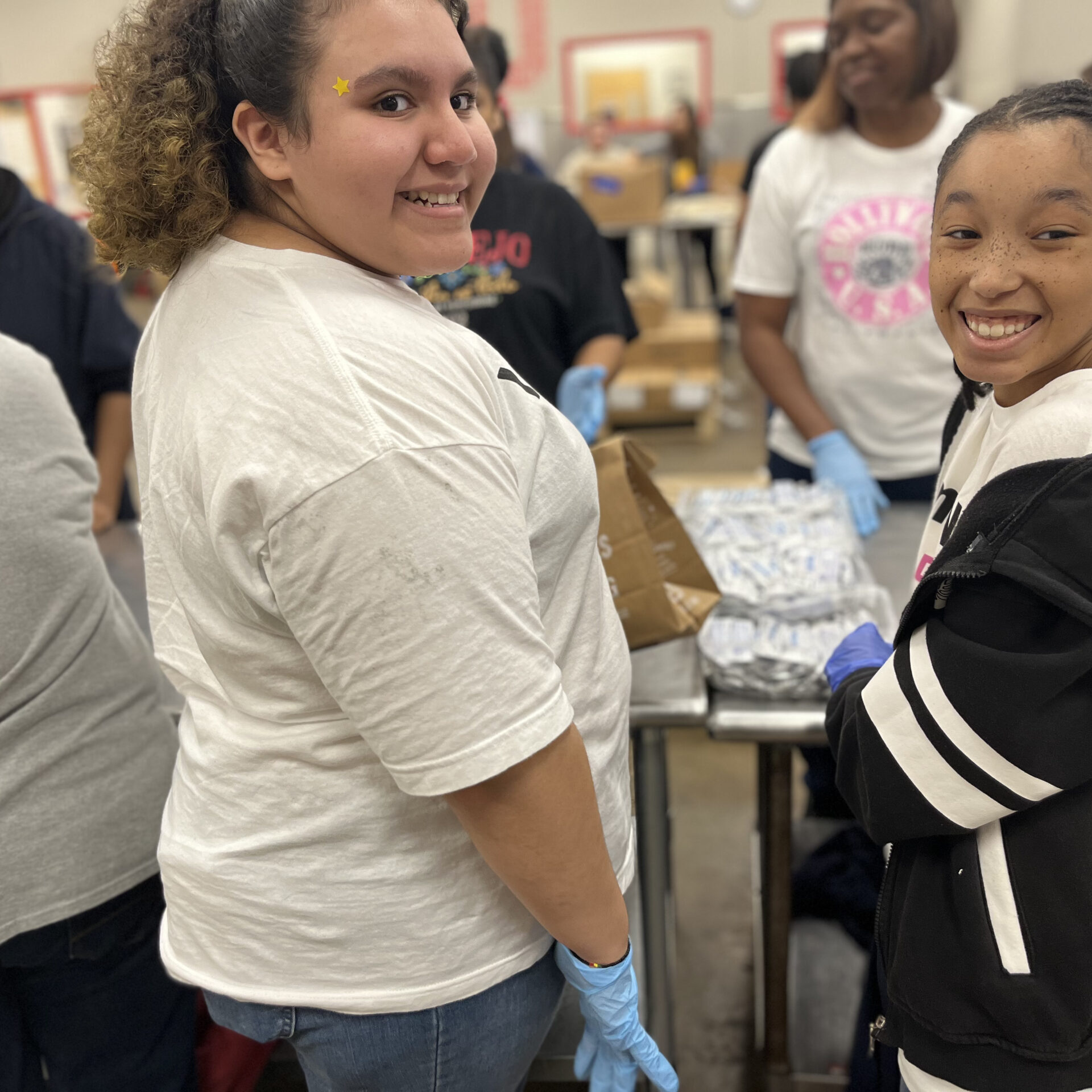 Six girls at a volunteer event, two are looking back at the photographer and smiling